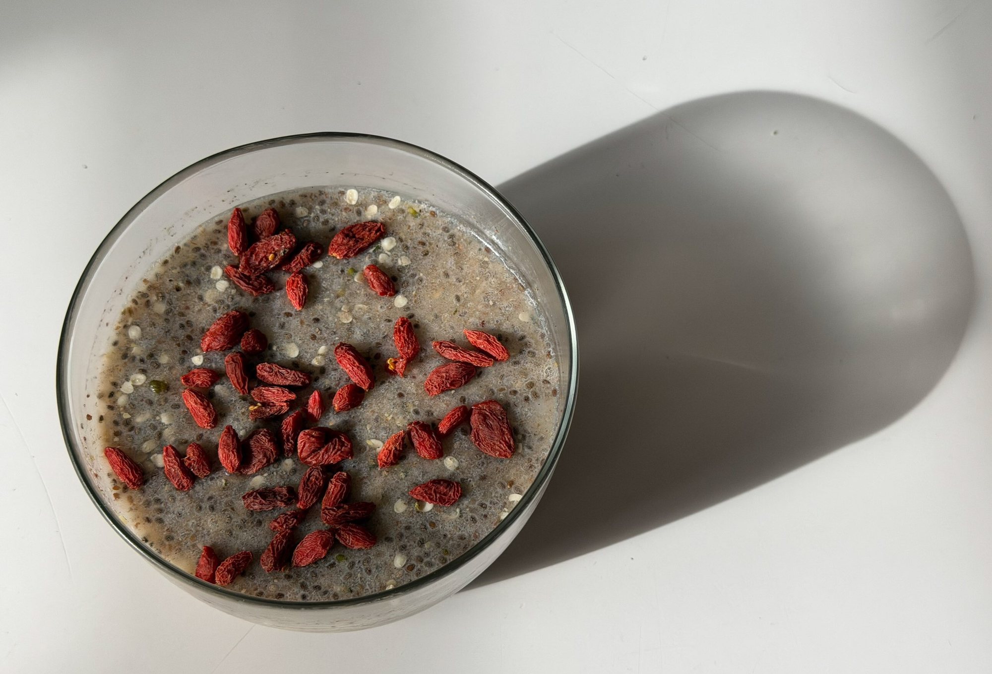 a glass of overnight sludge topped with goji berries, casting a long shadow